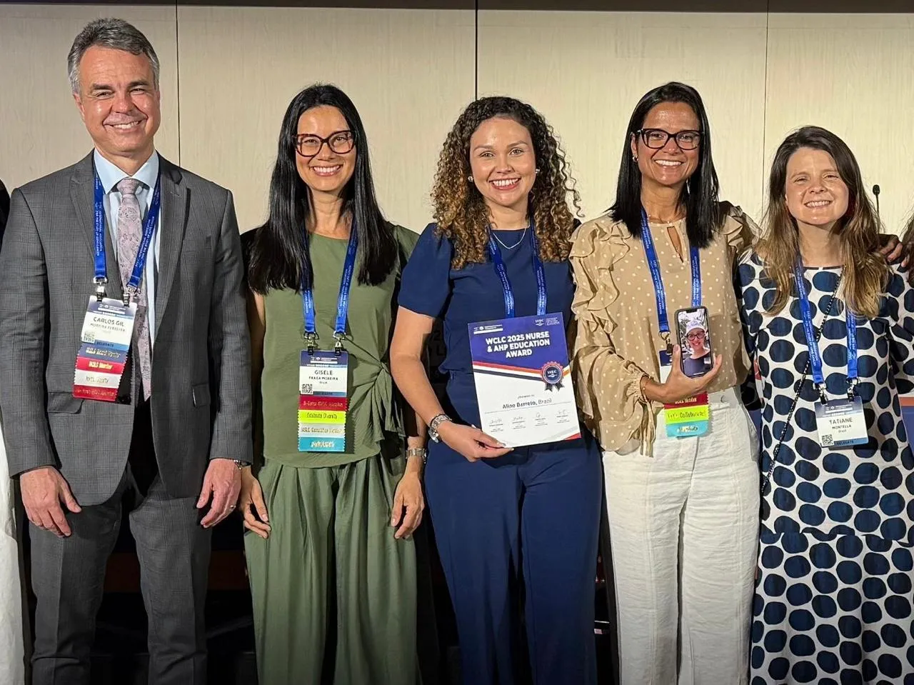 Aline Barcellos segurando o certificado do prêmio, ao centro de um grupo de cinco pessoas